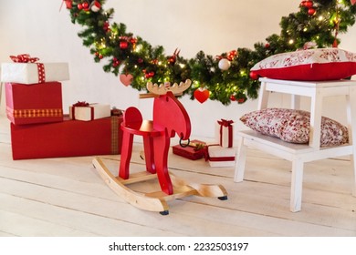 Studio or home Christmas interior with a big decorated wreath, rocking chair elk, present boxes, wooden white ladder chair with red pillows - Powered by Shutterstock