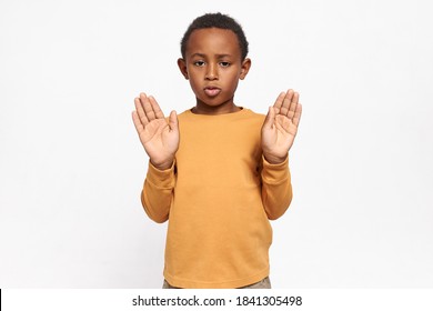 Studio image of serious confident African American schoolboy in sweatshirt reaching out his hands with palms open making stop gesture, saying No, Enough, expressing disagreement. Signs and symbols - Powered by Shutterstock