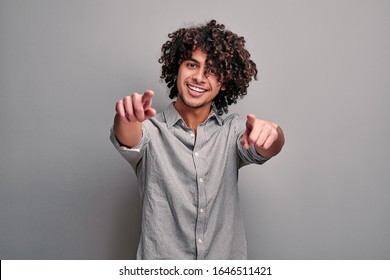 Studio image of young eastern curly boy poitns you with both hands.
