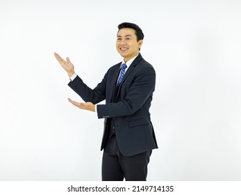 Studio Isolated Cutout Shot Of Asian Young Happy Male Businessman In Formal Business Suit Standing Smiling Holding Hands Showing Presenting Advertising Product On Empty Copy Space On White Background.