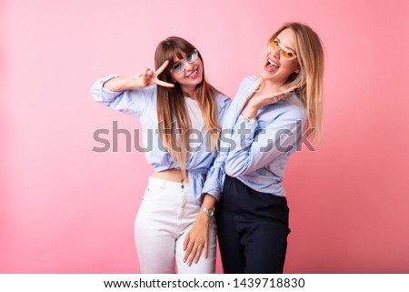 Studio lifestyle portrait of two best friends hipster girls send kisses,wearing stylish casual outfits, wearing shirt and white jeans.Two beautiful young women in casual clothes in studio.