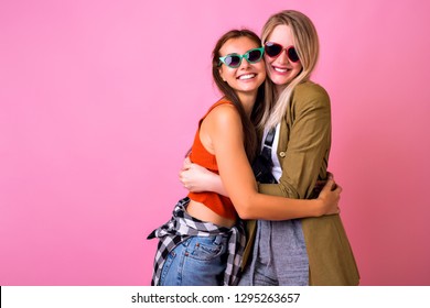 Studio lifestyle portrait of two stylish happy woman hugs and smiling, family relation goals, casual fashion outfits , vintage sunglasses, pink background.