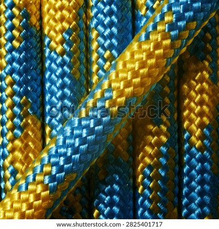Studio macro close up of bright blue and golden yellow braided synthetic rope featuring detailed nylon fiber texture, diagonal crossing pattern, vivid color contrast, fill frame background composition for outdoor climbing gear, marine equipment, and abstract industrial design.