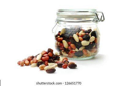 Studio Macro Of Mixed Nuts And Dried Fruit In A Jar Next To A Heap Of Nuts On A White Background With Soft Shadows. Copy Space.