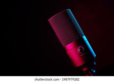 Studio microphone on dark background with copy space. Black professional condencer microphone with neon light. Podcast recording