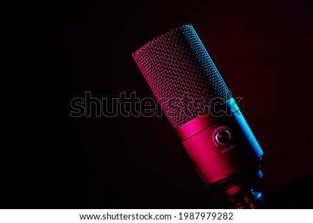 Studio microphone on dark background with copy space. Black professional condencer microphone with neon light. Podcast recording