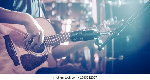 The Studio microphone records an acoustic guitar close-up, in a recording Studio or concert hall, with a drum set on a background in out-of-focus mode. Beautiful blurred background of colored lanterns - Powered by Shutterstock