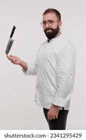 A studio photo of a bearded young chef holding a knife on his finger