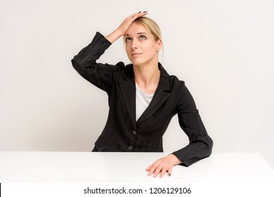 Studio Photo Of A Beautiful Blonde Girl Talking In A Business Suit On A White Background Sitting At The Table. She Is Sitting Right In Front Of The Camera, Smiling And Looking Happy.