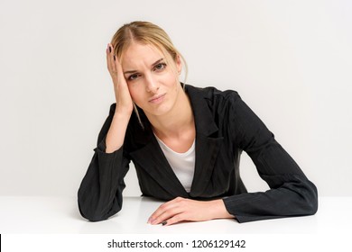 Studio Photo Of A Beautiful Blonde Girl Talking In A Business Suit On A White Background Sitting At The Table. She Is Sitting Right In Front Of The Camera, Smiling And Looking Happy.