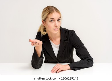 Studio Photo Of A Beautiful Blonde Girl Talking In A Business Suit On A White Background Sitting At The Table. She Is Sitting Right In Front Of The Camera, Smiling And Looking Happy.