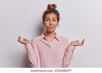 Studio photo of beautiful young confused European female on white background looking straight shrugging shoulders spreading palms with hesitation not knowing how to solve problem or answer question - Shutterstock ID 2332480377