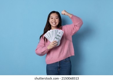 Studio photo with blue background of woman with a wad of banknotes raising the arm gesturing success