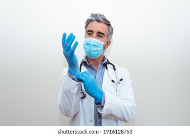 Studio Photo Of A Doctor With Mask In Uniform Putting On Blue Gloves With White Background