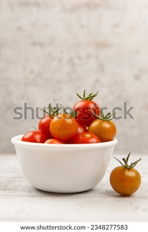 A studio photo of fresh ripe cherry tomatoes in a white bowl with one tomatoe on the side..