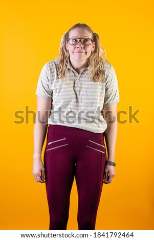 Studio photo of geeky blonde girl with glasses on yellow background.