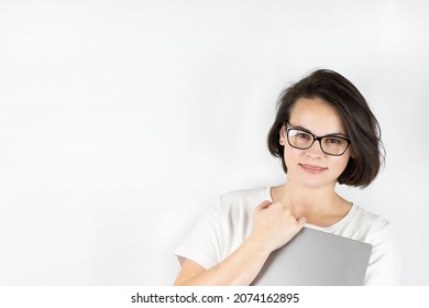 Studio photo on a white background of a beautiful smiling girl with dark hair in glasses with a laptop in her hands in front of her