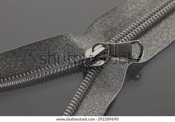 studio photography of gray silver zipper opened\
on a half to a gray\
surface