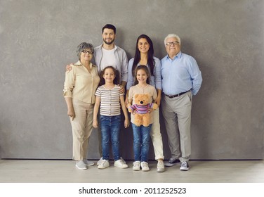 Studio photoshoot group portrait of happy big extended multi generational family. Cheerful mom, dad, grandma, grandpa and two little daughters with toy standing together, looking at camera and smiling - Powered by Shutterstock