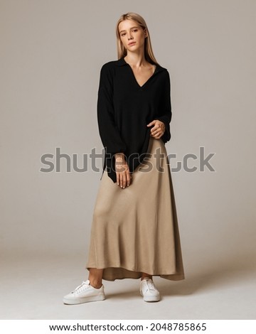 Studio photoshoot of a smiling young blond woman wearing casual clothing against a brown background.  Natural makeup and hairstyle.