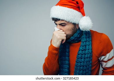 Studio Picture From A Young Man With Handkerchief. Sick Guy Isolated Has Runny Nose. Man Makes A Cure For The Common Cold. Winter Concept - Christmas Holiday. A Man Wearing A Santa Claus Hat