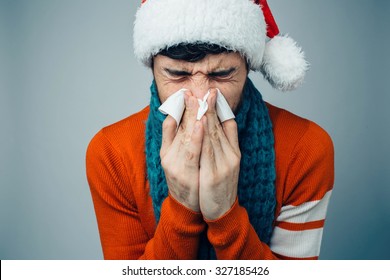 Studio Picture From A Young Man With Handkerchief. Sick Guy Isolated Has Runny Nose. Man Makes A Cure For The Common Cold. Winter Concept - Christmas Holiday. A Man Wearing A Santa Claus Hat