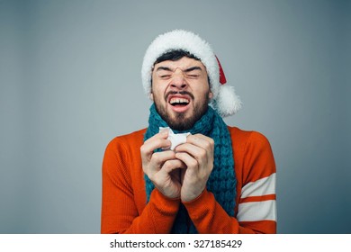 Studio Picture From A Young Man With Handkerchief. Sick Guy Isolated Has Runny Nose. Man Makes A Cure For The Common Cold. Winter Concept - Christmas Holiday. A Man Wearing A Santa Claus Hat