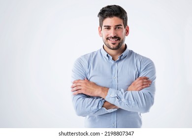 Studio portait of handsome man standing with arms crossed. Copy space. Male is wearing blue shirt against white background. He is smiling.