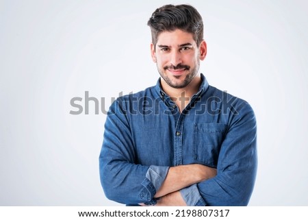 Studio portait of handsome standing with arms crossed. Copy space. Male is wearing denim shirt against white background. He is smiling.