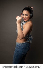 Studio Portrait Of A 40 Year Old Tunisian Woman Wearing Jeans And A Top. She Is Dancing And Wearing Black Headphones. The Background Is Grey. 