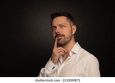 Studio Portrait Of A 40 Year Old Caucasian Man Wearing A White Shirt. The Background Is Black.  He Is Looking Away From The Camera. He Is Thinking.