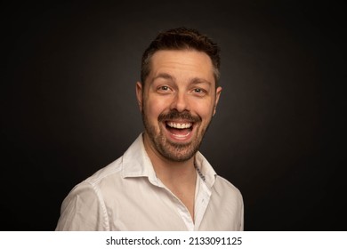 Studio Portrait Of A 40 Year Old Caucasian Man Wearing A White Shirt. The Background Is Black. He Has A Big Open Mouth Smile And Is Looking At The Camera.