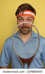 Studio Portrait Of A 40 Year Old Attractive Caucasian Man Wearing Vintage Clothing And Holding A Vintage Tennis Racket. The Studio Background Is Yellow.