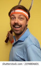 Studio Portrait Of A 40 Year Old Attractive Caucasian Man Wearing Vintage Clothing And Holding A Vintage Tennis Racket. The Studio Background Is Yellow.