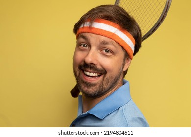 Studio Portrait Of A 40 Year Old Attractive Caucasian Man Wearing Vintage Clothing And Holding A Vintage Tennis Racket. The Studio Background Is Yellow.