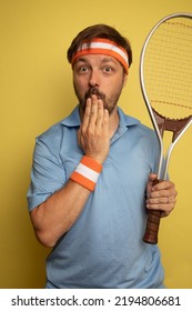 Studio Portrait Of A 40 Year Old Attractive Caucasian Man Wearing Vintage Clothing And Holding A Vintage Tennis Racket. The Studio Background Is Yellow.