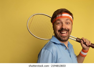 Studio Portrait Of A 40 Year Old Attractive Caucasian Man Wearing Vintage Clothing And Holding A Vintage Tennis Racquet. The Studio Background Is Yellow.