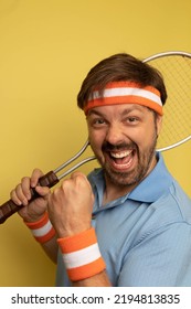 Studio Portrait Of A 40 Year Old Attractive Caucasian Man Wearing Vintage Clothing And Holding A Vintage Tennis Racquet. The Studio Background Is Yellow.