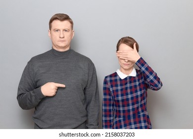 Studio Portrait Of Adult Couple, Serious Mature Man Is Pointing With Index Finger At Woman Covering Her Eyes With Hand, Looking Concentrated. Relationship Concept