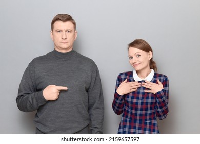 Studio Portrait Of Adult Couple, Serious Mature Man Is Pointing With Index Finger At Happy Woman, Looking Contented And Joyful, Smiling Cheerfully. Relationship Concept