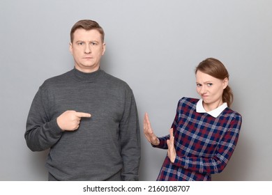 Studio Portrait Of Adult Couple, Serious Mature Man Is Pointing With Index Finger At Disgruntled Woman Raising Hands, Rejecting Something Unpleasant, Saying No Or Enough,  Relationship Concept