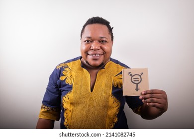 Studio Portrait Of An African Trans Person Holding A Cardboard With The Trans Symbol, He Is Dressed In A Traditional African Dress