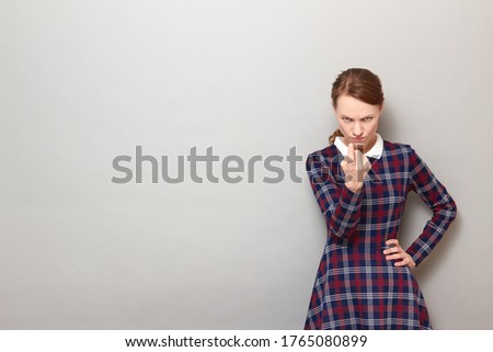 Studio portrait of angry disgruntled girl wearing checkered dress, beckoning someone with finger for serious talk, being dissatisfied with behavior, standing over gray background, with copy space Stock photo © 