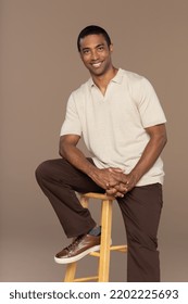 Studio Portrait Of Attractive Black Man In His 40s Sitting On A Stool And Smiling On Neutral Background