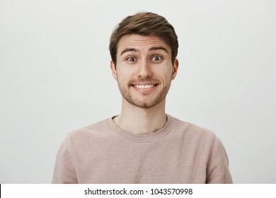 Studio portrait of attractive caucasian guy feeling awkward and confused, not knowing what to say and smiling nervously, standing against gray background, being in strange situation