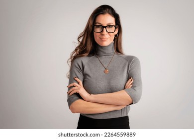 Studio portrait of an attractive middle aged woman with eyewear wearing turtleneck sweater and black pants while standing at isolated grey background. Copy space. Studio shot.
