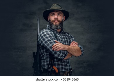 Studio portrait of a bearded hunter holds a rifle.