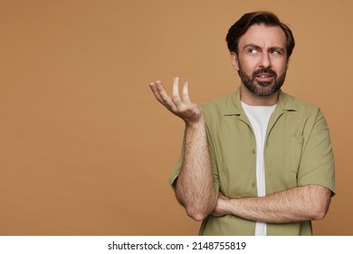 Studio Portrait Of Bearded Man Posing Over Beige Background Raised His Hand With Confused Facial Expression