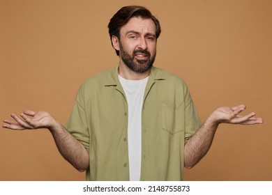 Studio Portrait Of Bearded Man Posing Over Beige Background Holding Copy Space On Both Palms With Confused Facial Expression