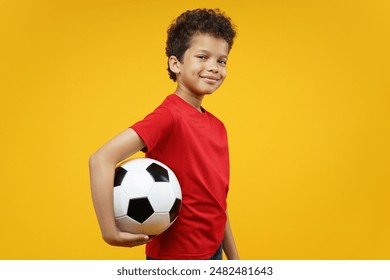 Studio portrait of beautiful African American boy kid posing with a soccer ball in hand, isolated over bright colored orange yellow background.                                - Powered by Shutterstock